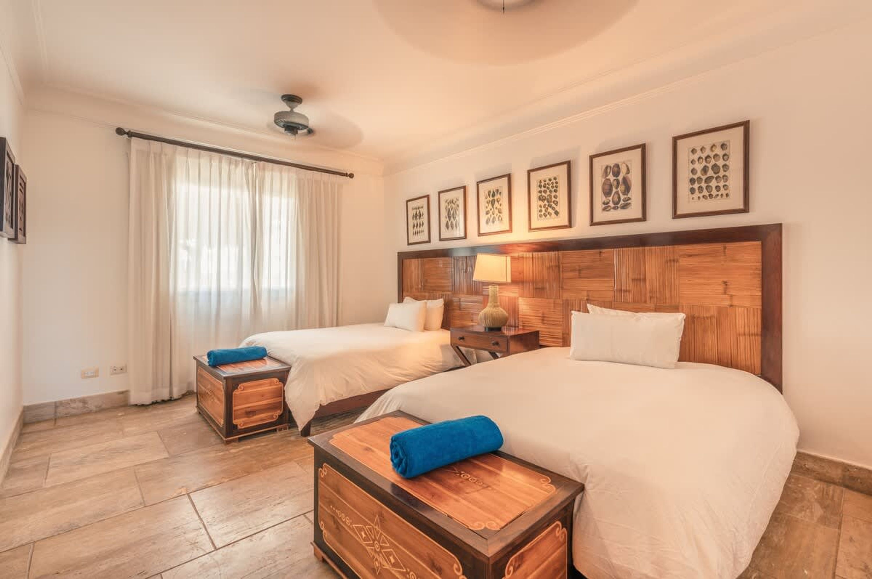 A hotel room with two beds, a wooden headboard, a nightstand, and a window with curtains.