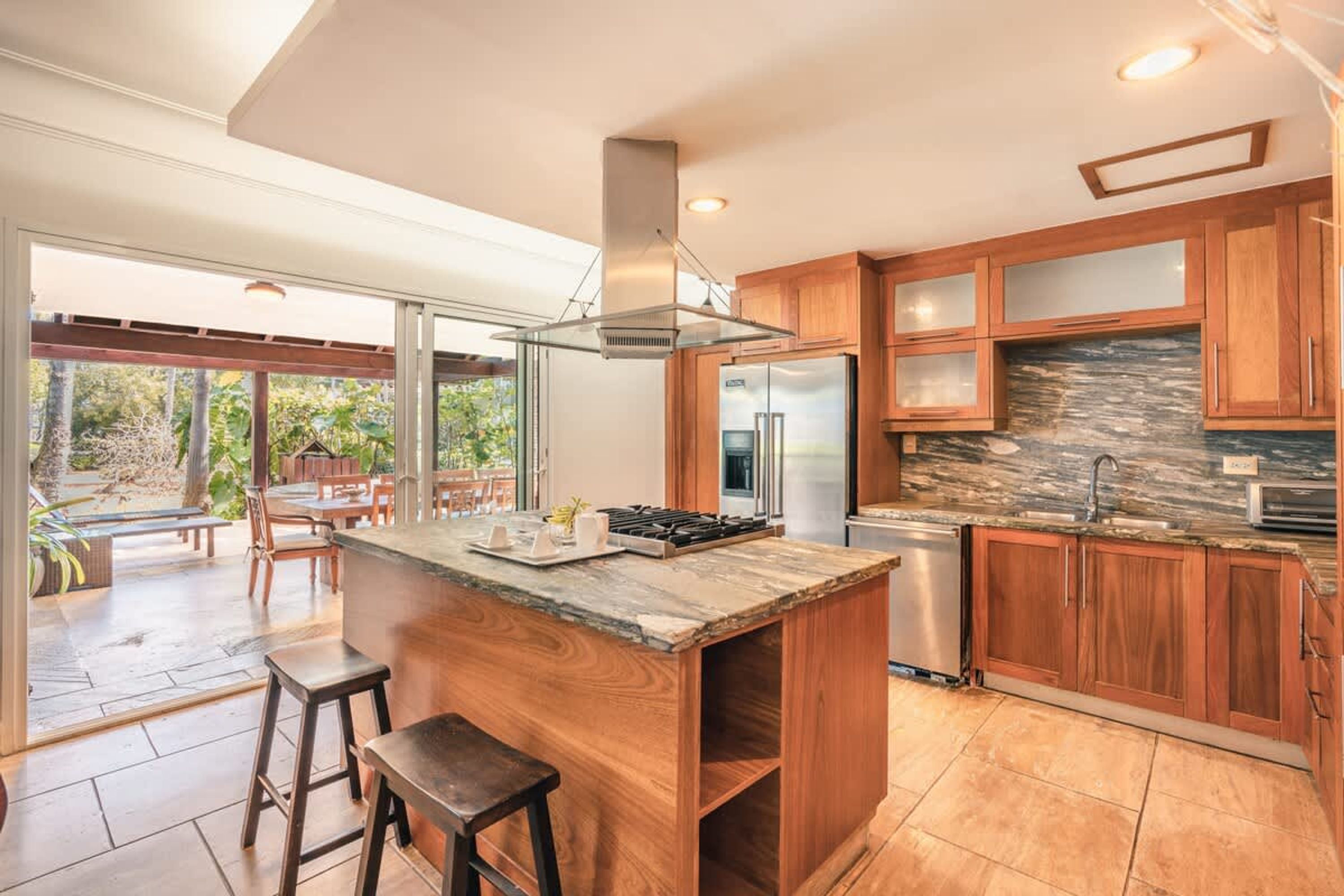 A modern kitchen with a central island, wooden cabinets, and a stone backsplash.