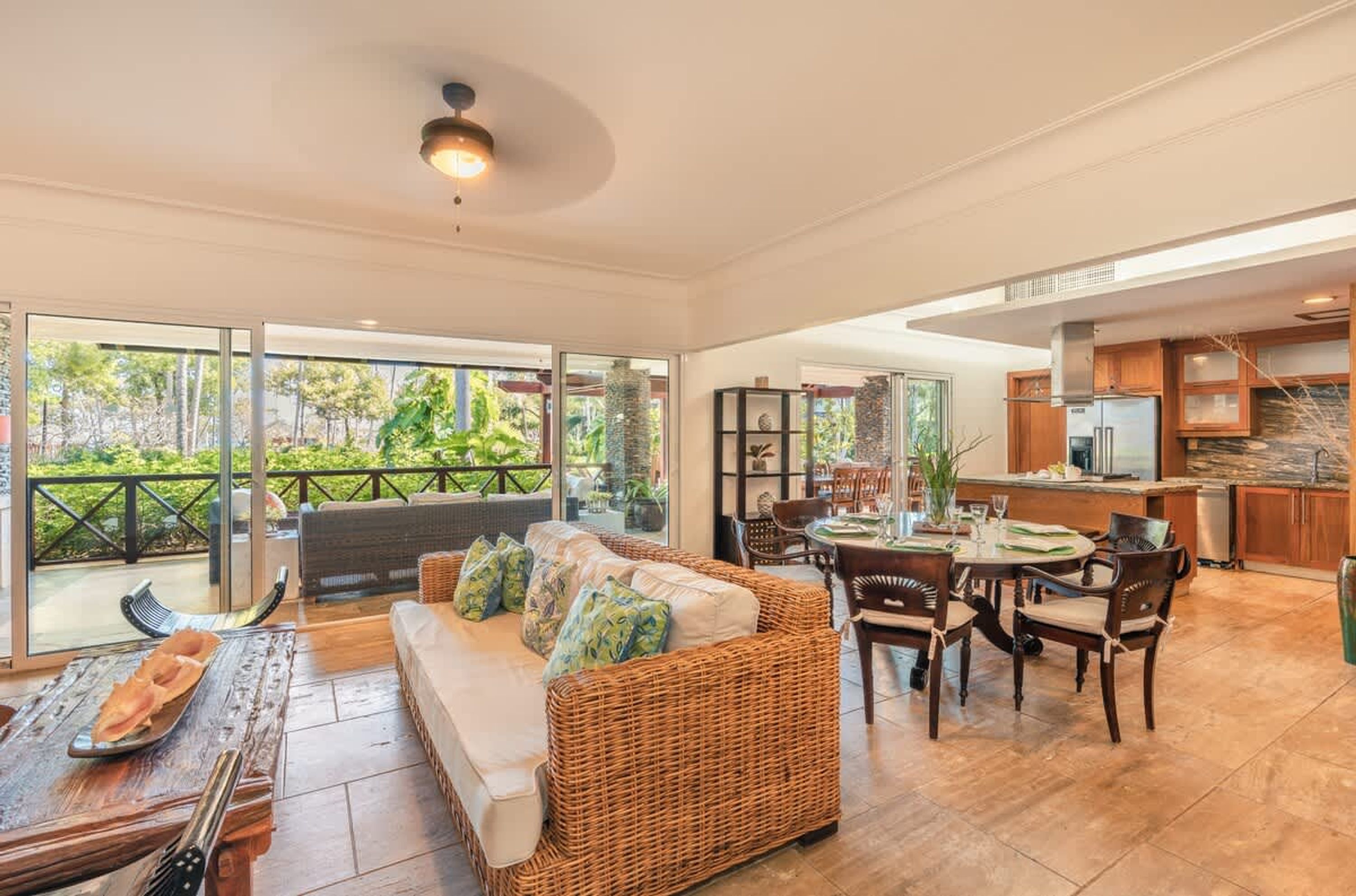 A spacious living area with a sofa, dining table, and chairs, a kitchen area, and large sliding glass doors leading to a balcony.