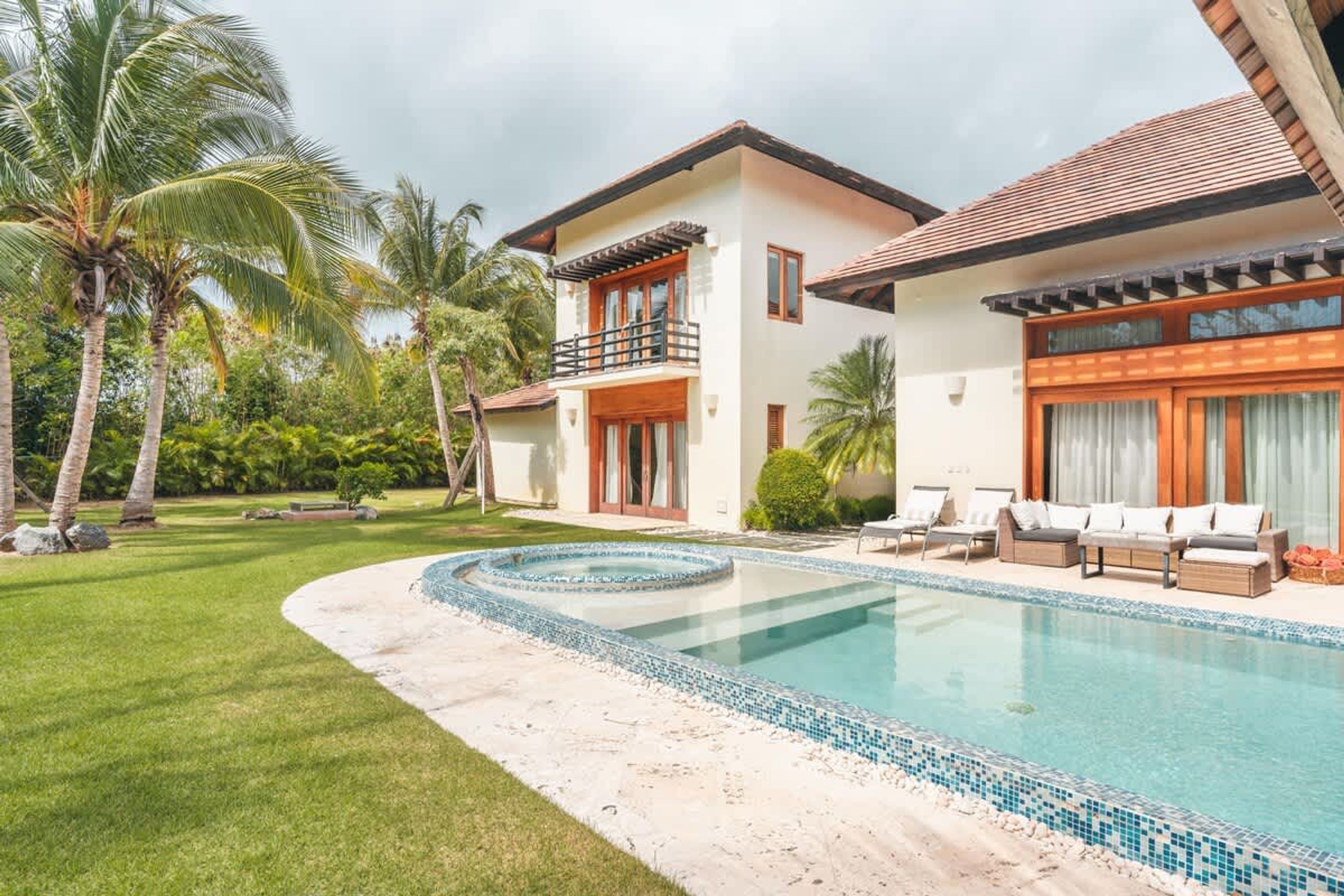 A two-story house with a swimming pool, surrounded by palm trees and a well-maintained lawn.