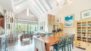 A spacious dining area with a wooden table and chairs, a kitchen with a built-in cabinet, and large windows offering a view of the outdoors. - Retreat Apartment With 3 Bedrooms in Portillo Nf (Las Terrenas)