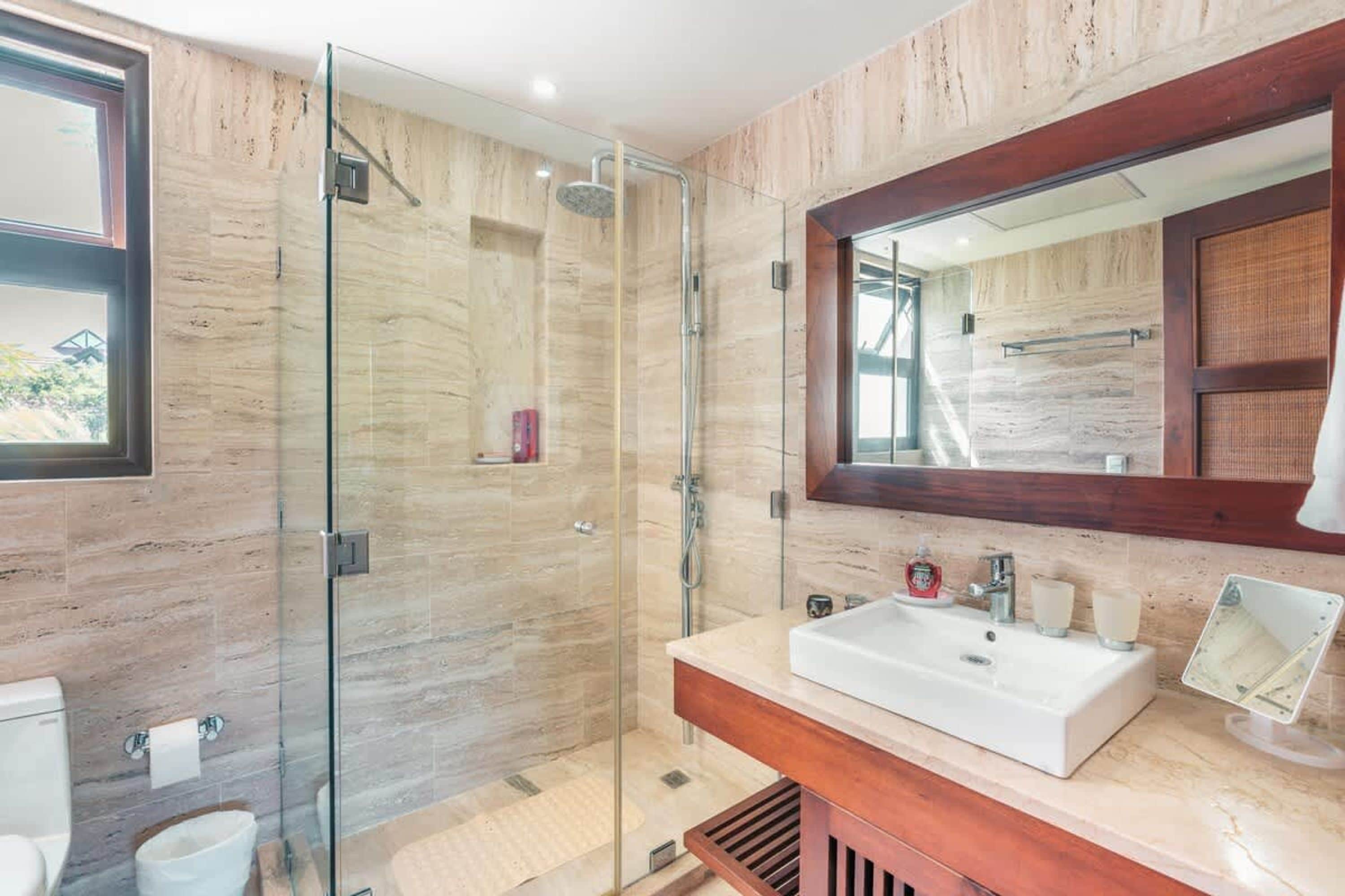 Een moderne badkamer met een glazen douchecabine, een grote spiegel en een witte wastafel.
