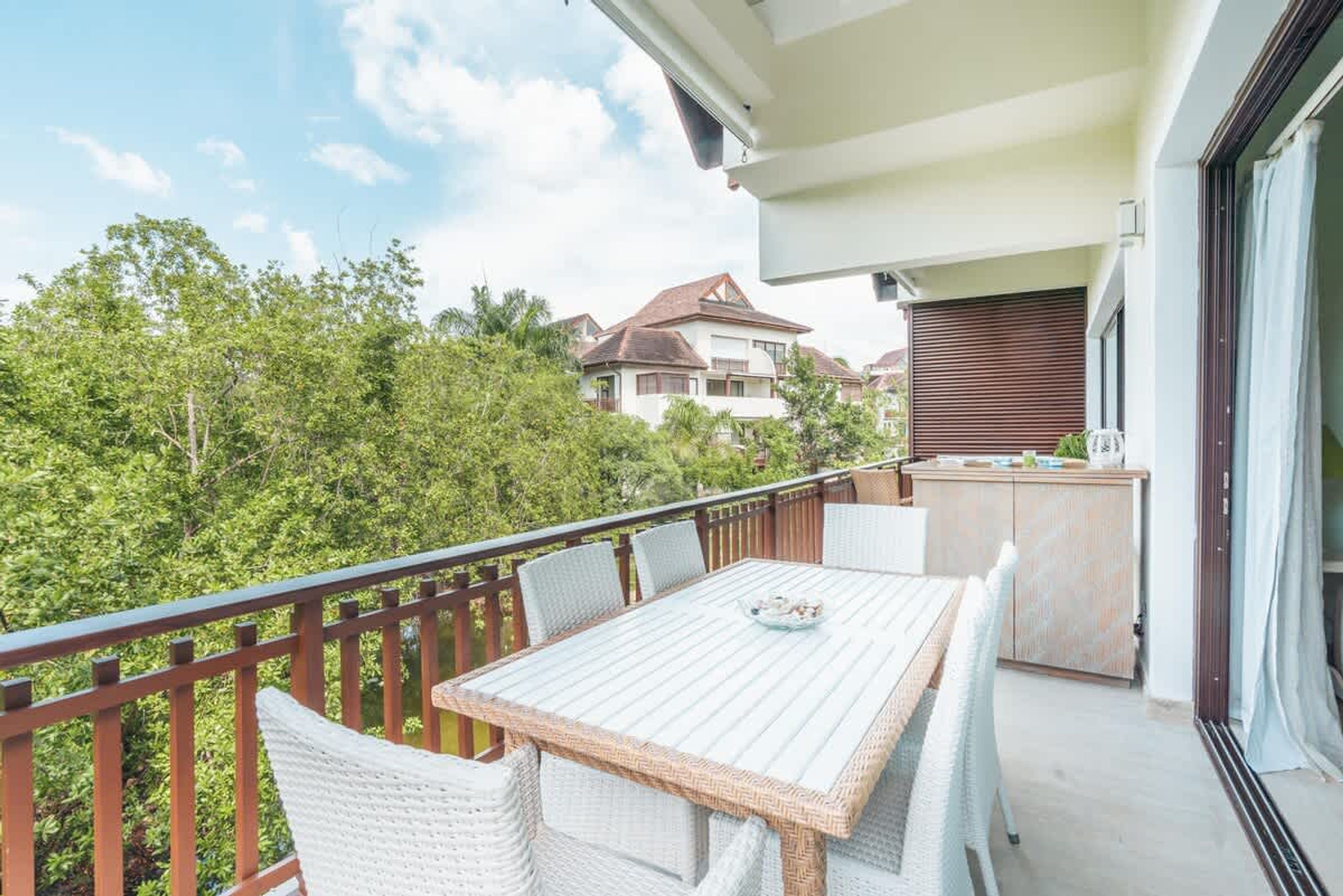 A balcony with a dining table and chairs, a wooden cabinet, and a view of neighboring houses and trees.
