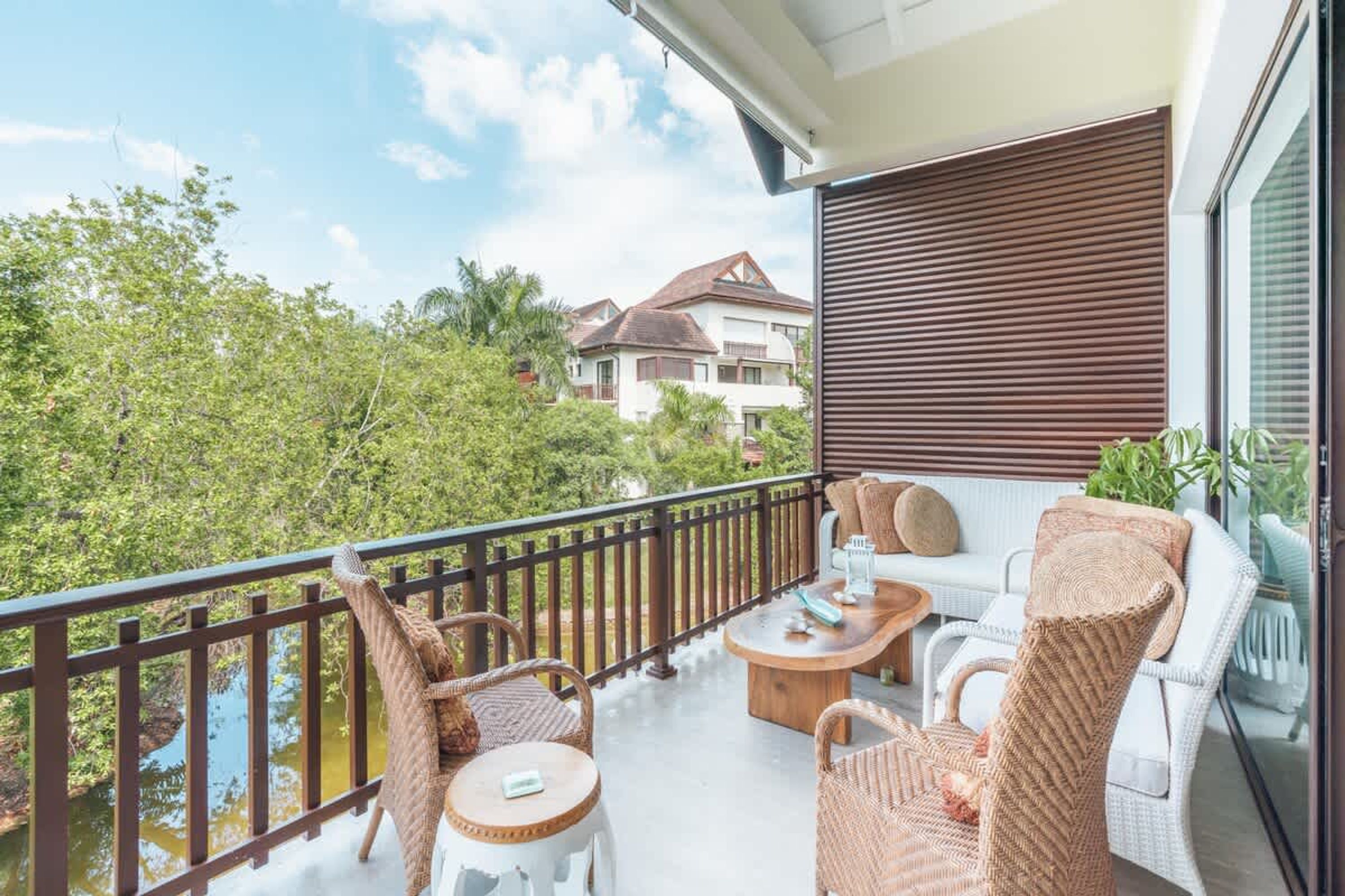 A balcony with wicker furniture, a wooden table, and a view of a lake and buildings.