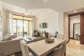 A modern living room with a sofa, dining table, and TV. - Elegant 1br Casa de Campo Retreat w Garden Views (La Romana)
