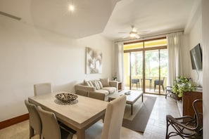A modern living room with a dining area, a sofa set, a coffee table, and a television. - Elegant 1br Casa de Campo Retreat w Garden Views (La Romana)