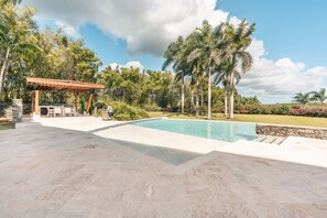 A swimming pool with a pergola, outdoor seating, and palm trees. - Elegant 1br Casa de Campo Retreat w Garden Views (La Romana)