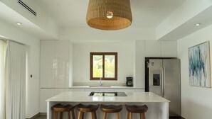 A modern kitchen with a central island, bar stools, stainless steel appliances, and a large window. - Modern Villa With Jacuzzi Pool View in Monterrico (Taxisco)