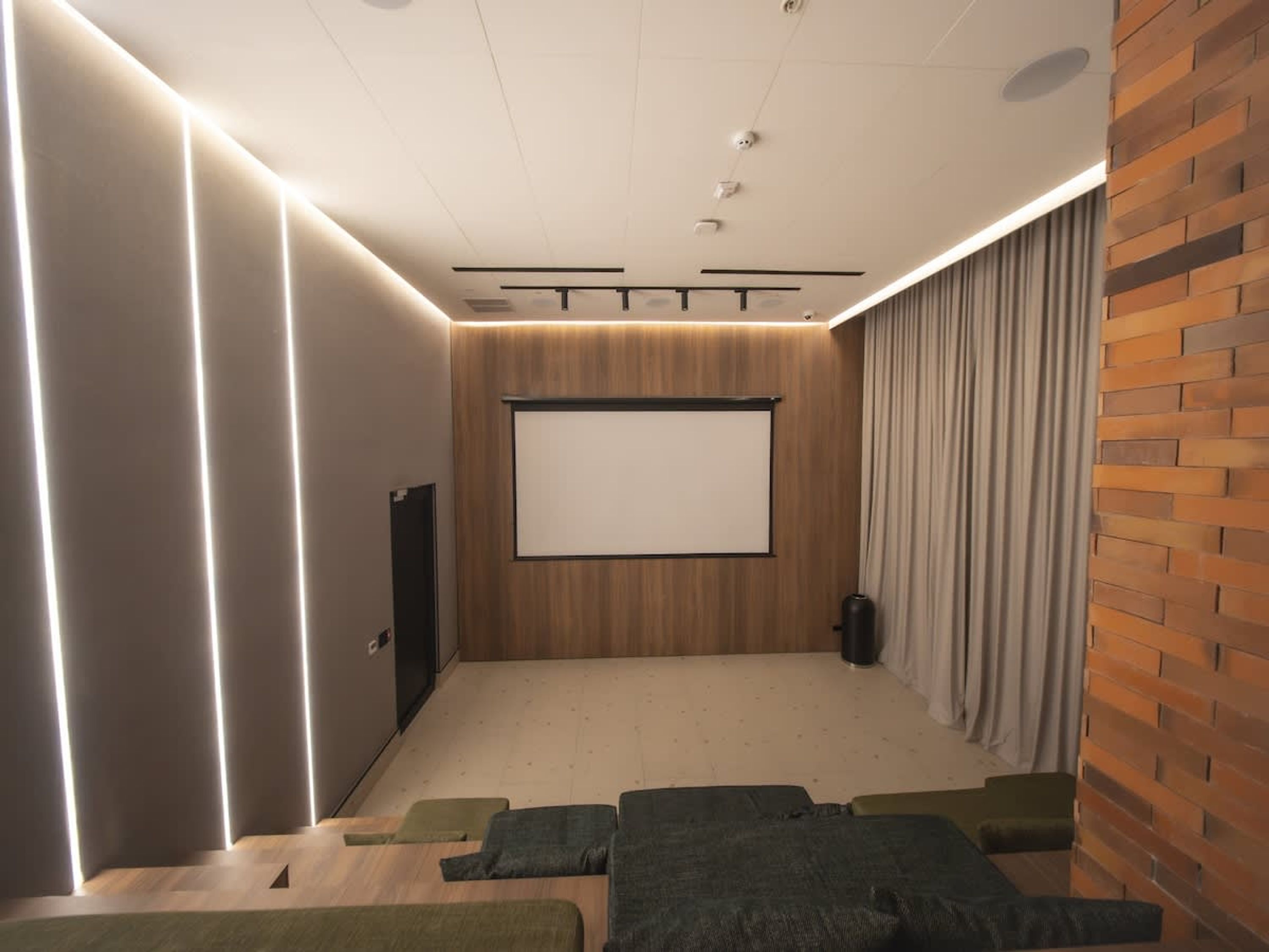 A modern home theater room with a large screen, comfortable seating, and a brick accent wall.