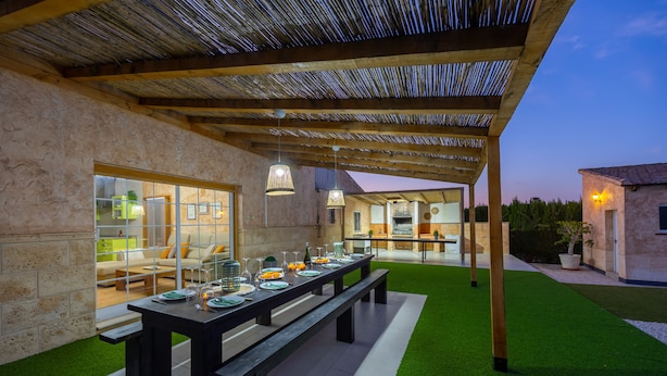 An outdoor dining area with a long table set for a meal, surrounded by a covered patio with a thatched roof. - Sunnyvalley by Fidalsa (Dolores)