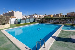 A rectangular swimming pool with a clear blue water, surrounded by a green lawn and a low stone wall. - Blue Lagoon by Fidalsa (Torrevieja)