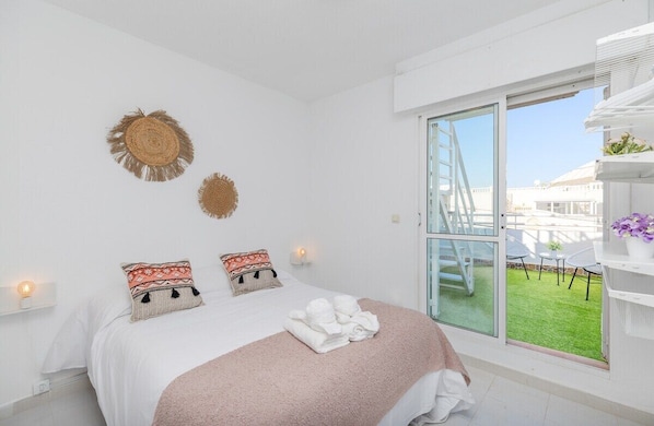 A modern hotel room with a large bed, two wall-mounted decorative items, a balcony with a view, and a white shelving unit with plants. - Blue Lagoon by Fidalsa (Torrevieja)