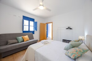 Une chambre à coucher comprenant un lit, un canapé, un ventilateur de plafond, une fenêtre avec des volets bleus et une porte.