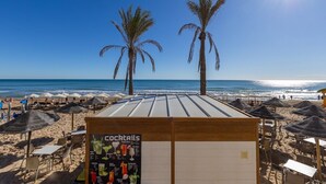 A beachside bar with a menu board, palm trees, and beach umbrellas. - Fidalsa Bay View Romance (Guardamar del Segura)