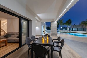 A modern outdoor dining area with a pool, a staircase, and a glass door leading to a living space. - Palm Breeze Villa by Fidalsa (Catral)