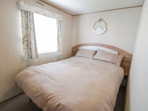 A bedroom with a bed, curtains, a headboard, and a wall decoration. - 51 Silverbirch Way (Rhyl)