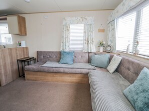 Un salon confortable avec un canapé, des coussins, une petite table et une fenêtre avec des rideaux.