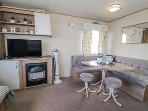 A compact living space with a television, kitchenette, seating area, and a mirror. - 51 Silverbirch Way (Rhyl)