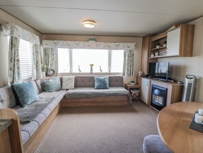 Ein gemütliches Wohnmobil-Interieur mit einer Sitzecke, einem kleinen Tisch, einem Fernseher und einer Küchenzeile.