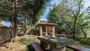 A stone-built outdoor kitchen with a stone table and benches, surrounded by trees. - Fidalsa Paradise Point (Cabezon de Liebana)