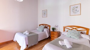 A room with two beds, wooden headboards, a wooden nightstand, a small table with a lamp, and two framed floral artworks on the walls. - Fidalsa Paradise Point (Cabezon de Liebana)
