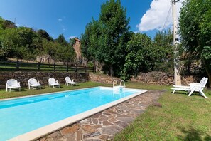 Une piscine rectangulaire bordée de pierres, avec des chaises longues blanches.