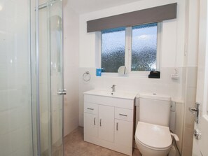 Et badeværelse med et glasbadeværelse, en hvid vask med et spejl og et toilet.