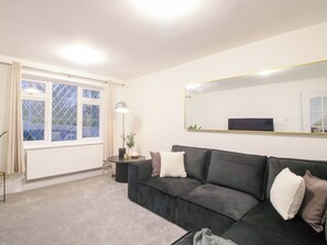 En moderne stue med en sort lædersofa, et rundt sofabord, en gulvlampe og et stort spejl på væggen.