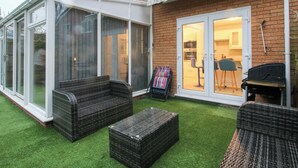 A patio with wicker furniture, a glass-enclosed area, and a brick house. - Beau Jardin (Telford)