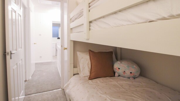 A bedroom with a bunk bed, a door leading to another room, and a visible bathroom in the background. - Beau Jardin (Telford)