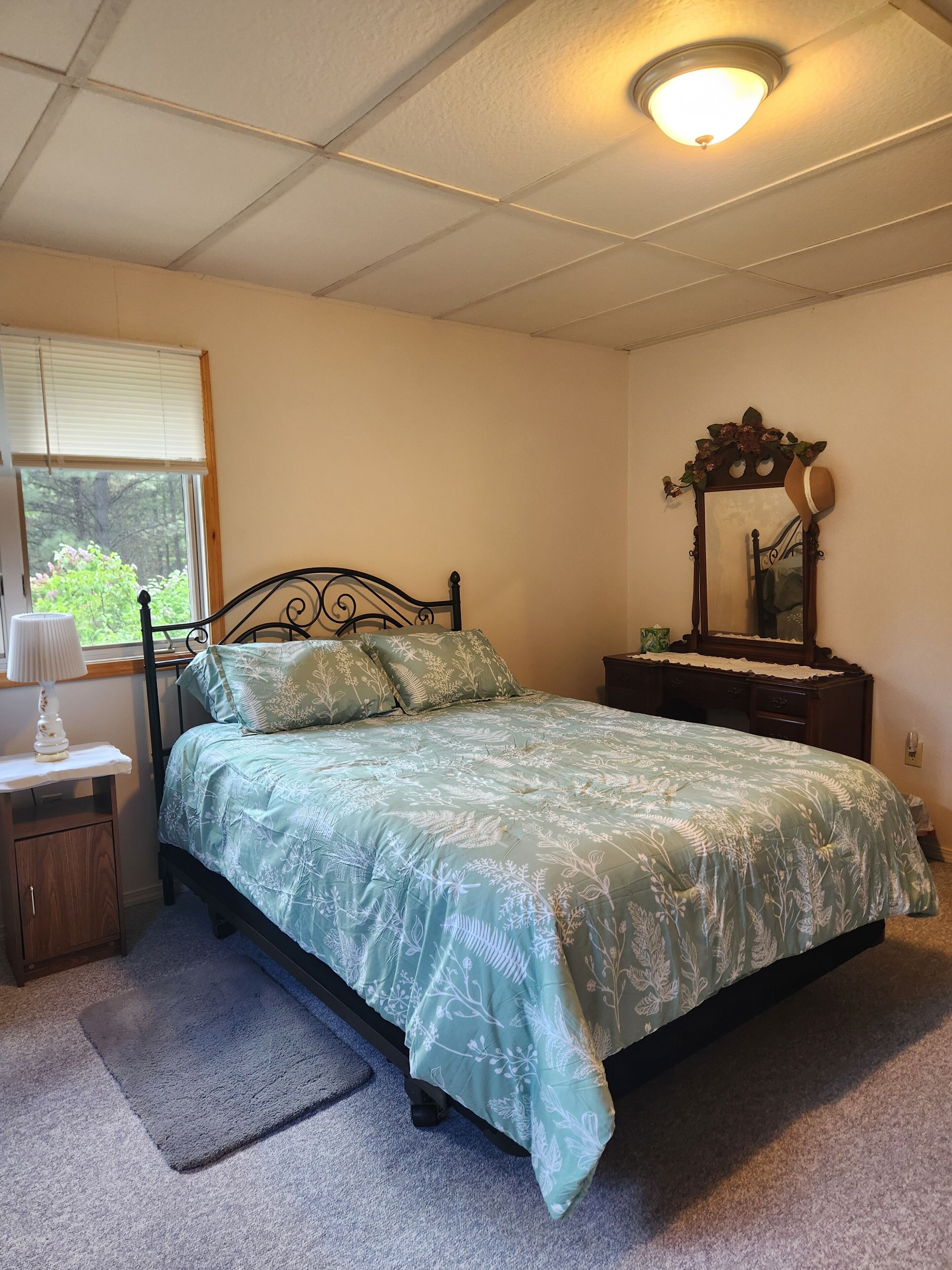 Un dormitorio con cama, mesita de noche, cómoda, espejo y ventana con persianas.