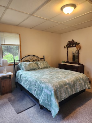Un dormitorio con cama, mesita de noche, cómoda, espejo y ventana con persianas.
