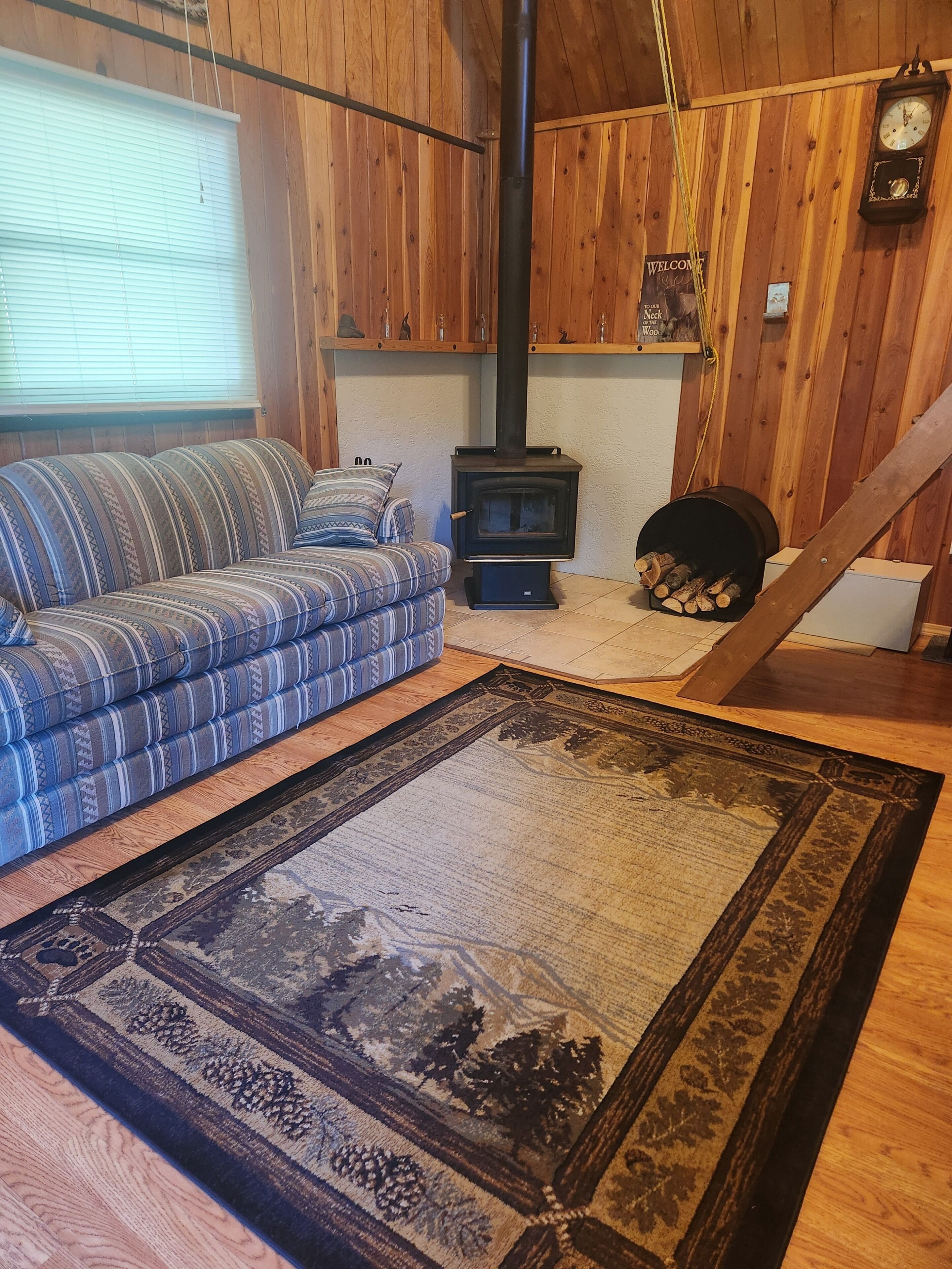 A cozy room with a sofa, a rug, a wood-burning stove, and a clock on the wall.