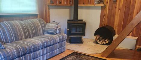 A cozy room with a sofa, a rug, a wood-burning stove, and a clock on the wall.