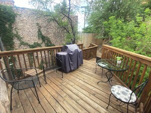 A wooden deck with two metal chairs and a table, a covered grill, and a stone wall with greenery. - Iron Rider Studio - Couples Motorcycle Theme Loft Walkable Downtown Hot Springs (Hot Springs)