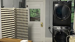 A laundry room with two stacked front-loading washers, a wooden table, a striped partition, and a white door. - Iron Rider Studio - Couples Motorcycle Theme Loft Walkable Downtown Hot Springs (Hot Springs)