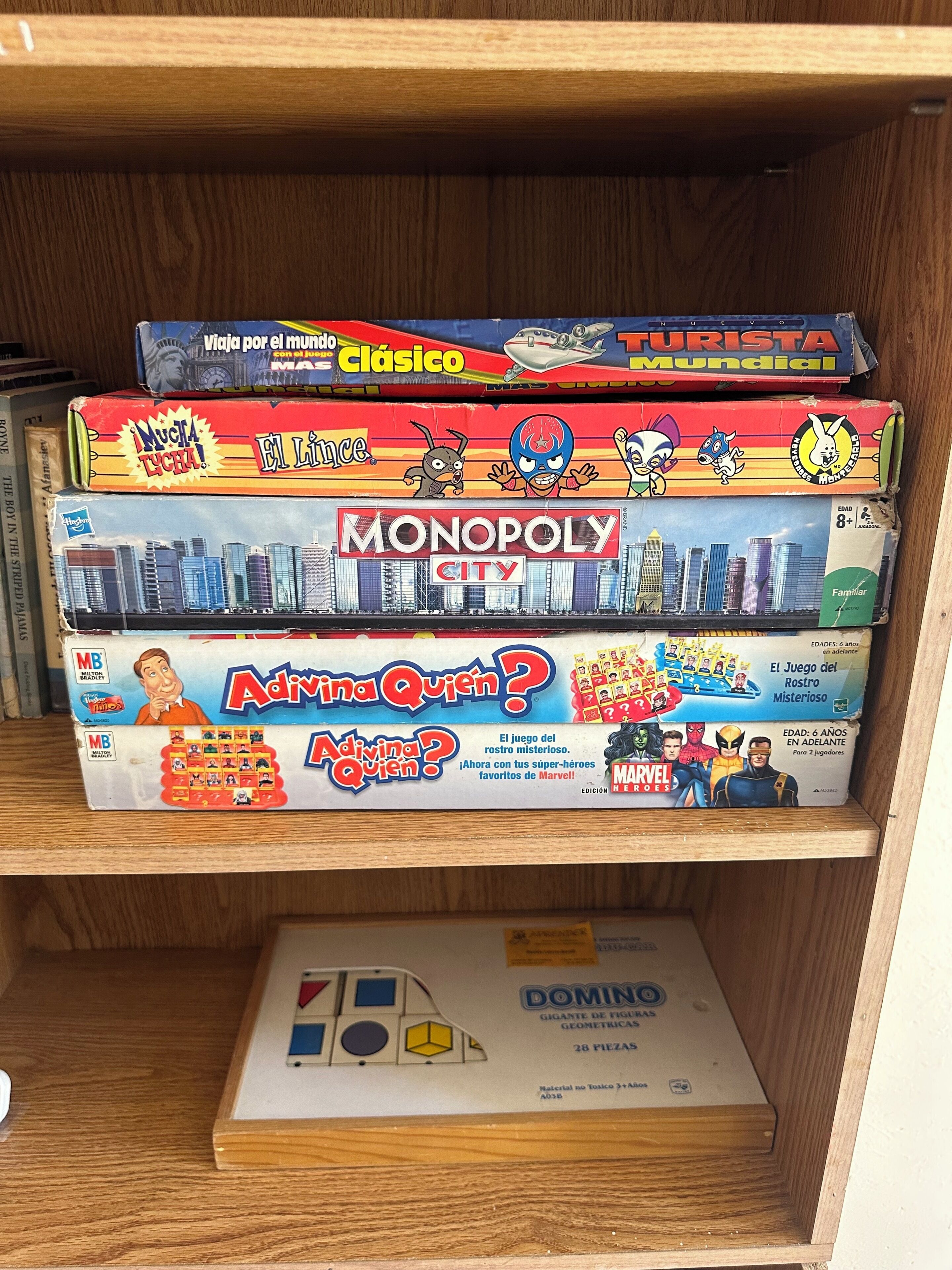 A shelf with various board games including Monopoly City, Adivina Quem?, and others.