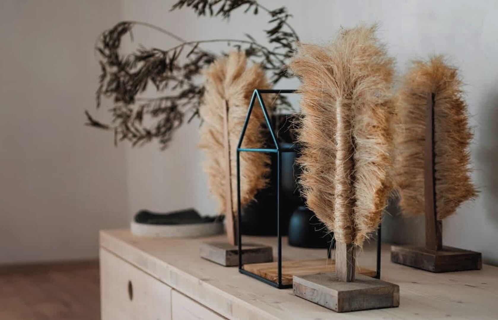 Een houten dressoir met daarboven drie hoge, slanke, beige decoratieve objecten op metalen voetstukken.