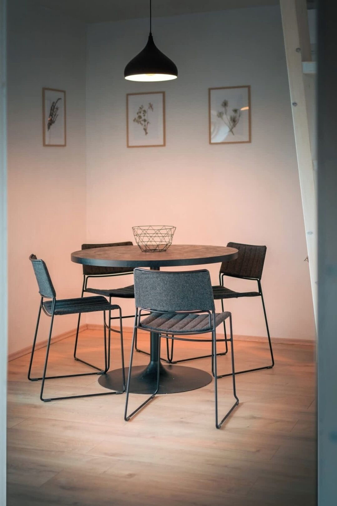Een eethoek met een ronde tafel, vier stoelen, een mand van draad en een hanglamp.