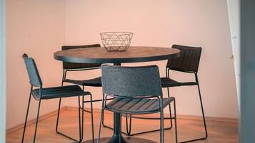 Een eethoek met een ronde tafel, vier stoelen, een mand van draad en een hanglamp.