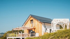 A modern wooden cabin with a balcony, a white structure with circular cutouts, and a clear sky.