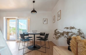 Un comedor moderno con una mesa redonda, cuatro sillas, una lámpara colgante y un ventanal con vistas.