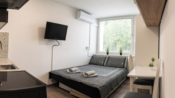 A compact room with a bed, a small table, a TV, and an air conditioning unit.