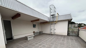 A rooftop terrace with a metal staircase, a door, and a small bench.