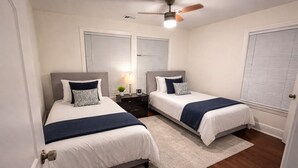 A bedroom with two beds, a ceiling fan, a nightstand with a lamp, and a window with blinds. - 12 Min to Mercedes-Benz Stadium  2BR Sleeps 5  4 Min to MARTA (East Point)