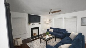 A living room with a fireplace, a blue sofa, a coffee table, and a ceiling fan. - 12 Min to Mercedes-Benz Stadium  2BR Sleeps 5  4 Min to MARTA (East Point)