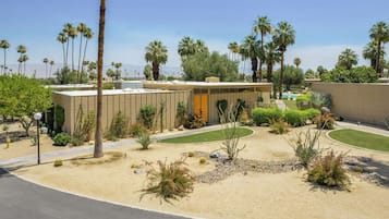 A modern building with a pool, surrounded by palm trees and landscaped gardens.