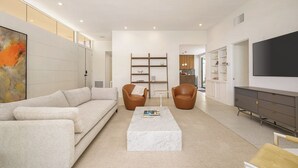 Een moderne woonkamer met een witte bank, twee leren fauteuils, een marmeren salontafel en een boekenkast.