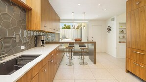 Een moderne keuken met houten kastjes, een roestvrijstalen spoelbak en een bar met krukken.