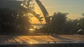 Een zwembad met betegelde rand, een zonsondergang op de achtergrond en een silhouet van een gebouw.